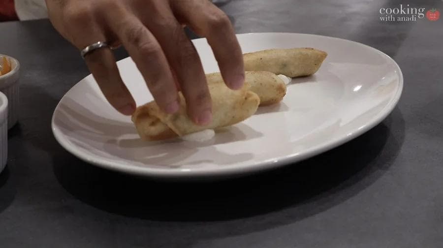 Hand arranging crispy mashed potato spring rolls on a white plate in a stacked pattern.