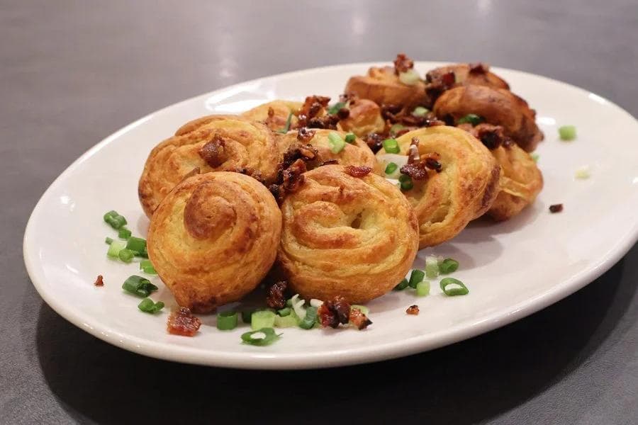 Golden air fryer mashed potato pinwheels topped with crispy bacon bits and green onions on a white plate.
