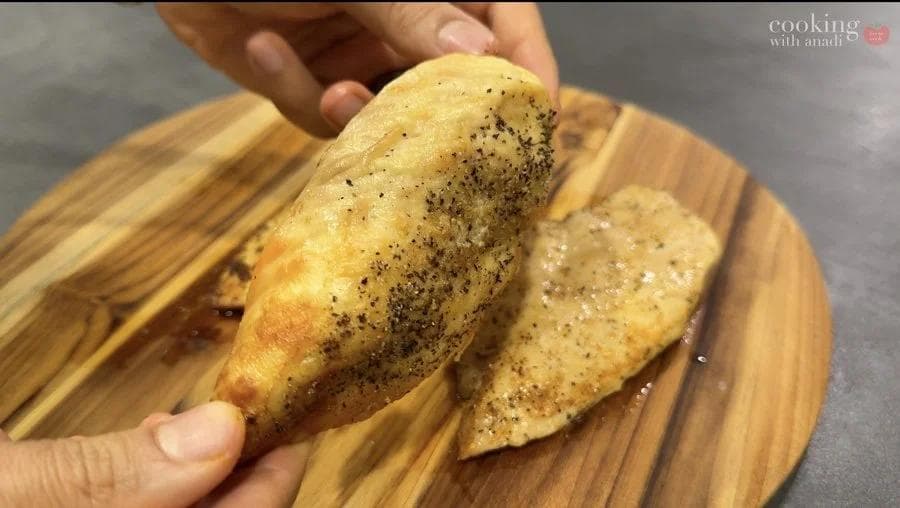 Oil-coated chicken breast seasoned with black pepper, held up to display golden-brown exterior before cooking.