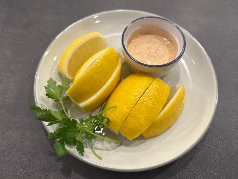 Lemon wedges and cilantro garnish with a small bowl of dipping sauce on a white plate.