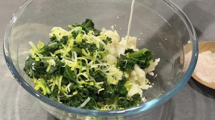 Mashed potatoes mixed with shredded green onions and chives in a glass bowl.