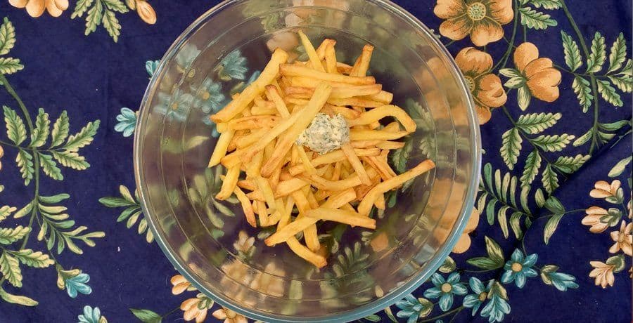 Shredded cheddar cheese and garlic butter being mixed with golden air fryer fries in a glass bowl.
