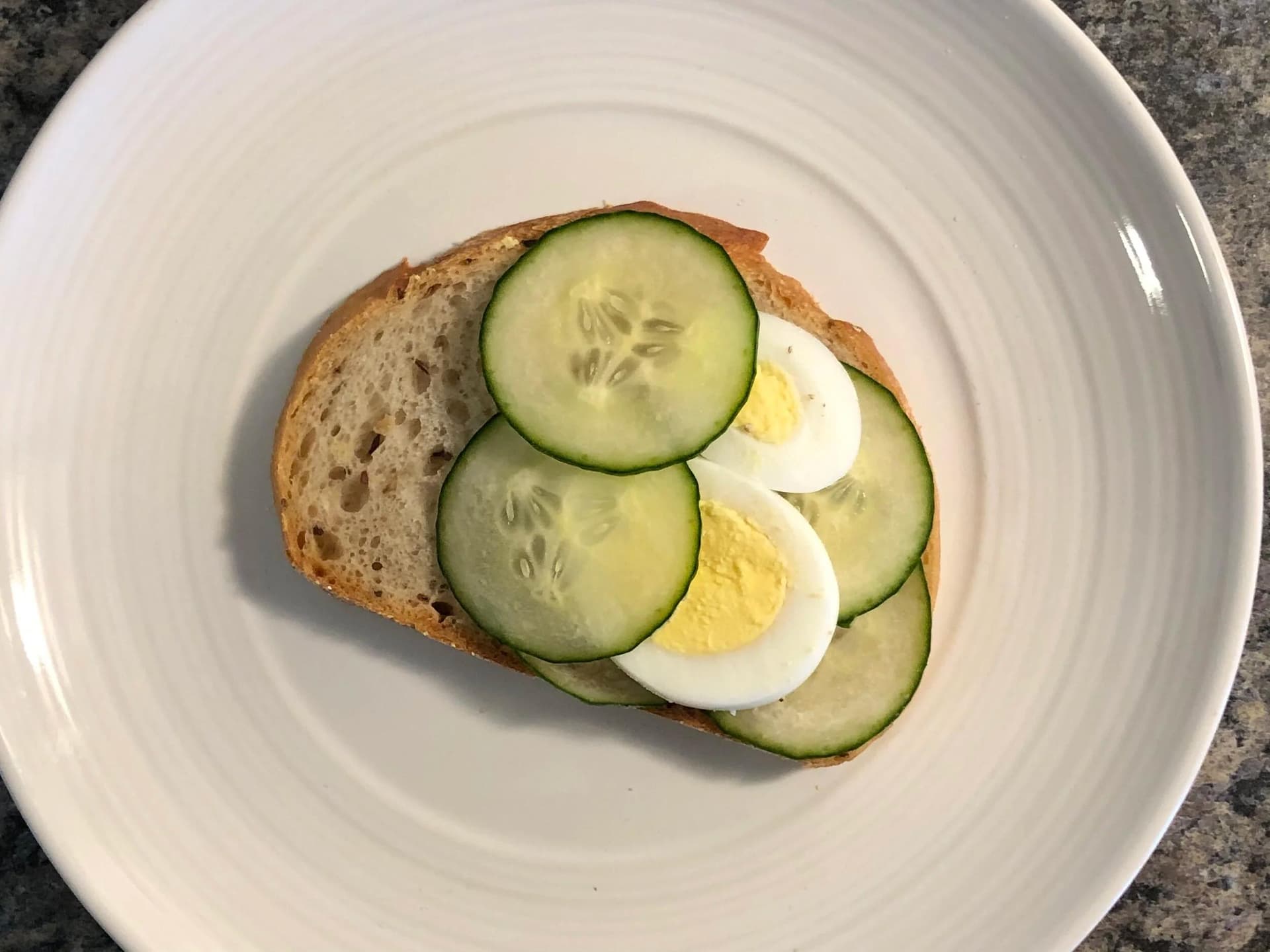 Toasted bread topped with overlapping cucumber slices and halved boiled eggs on a white plate.