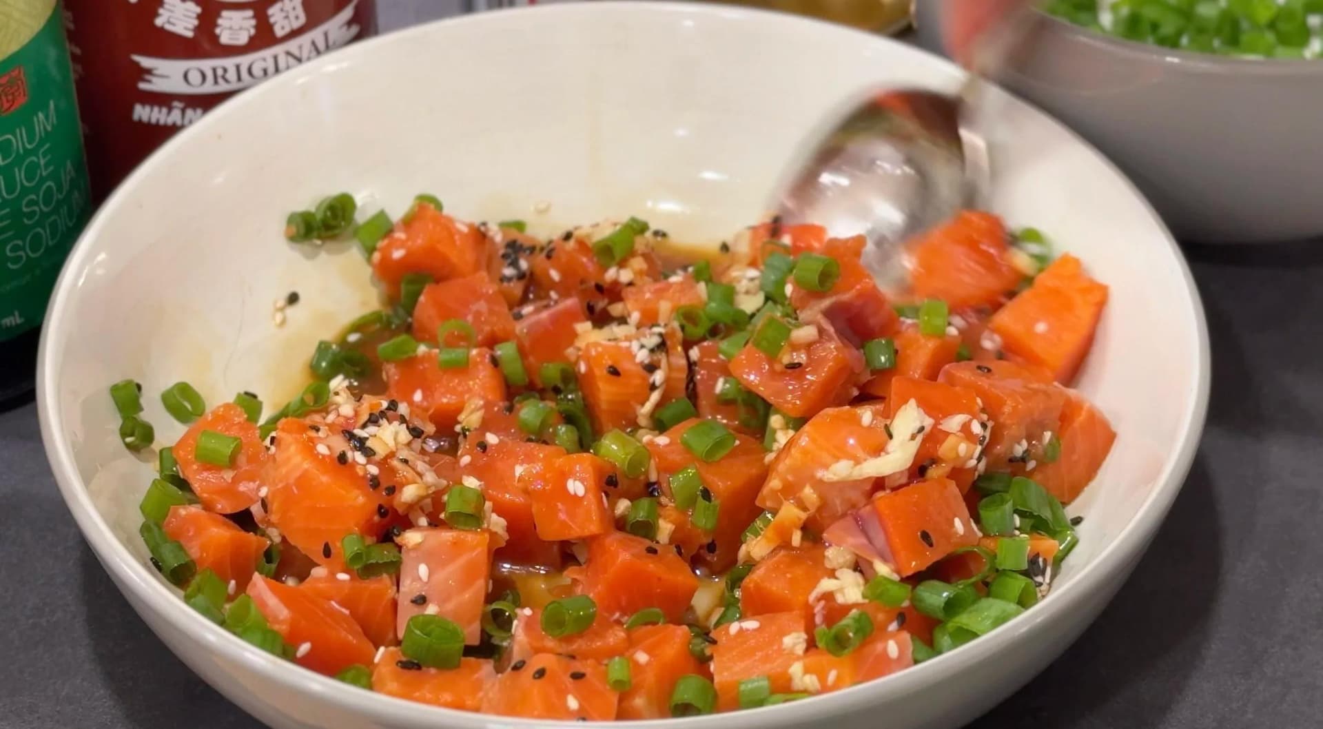 Marinated salmon poke in a white bowl garnished with sesame seeds and green onions.