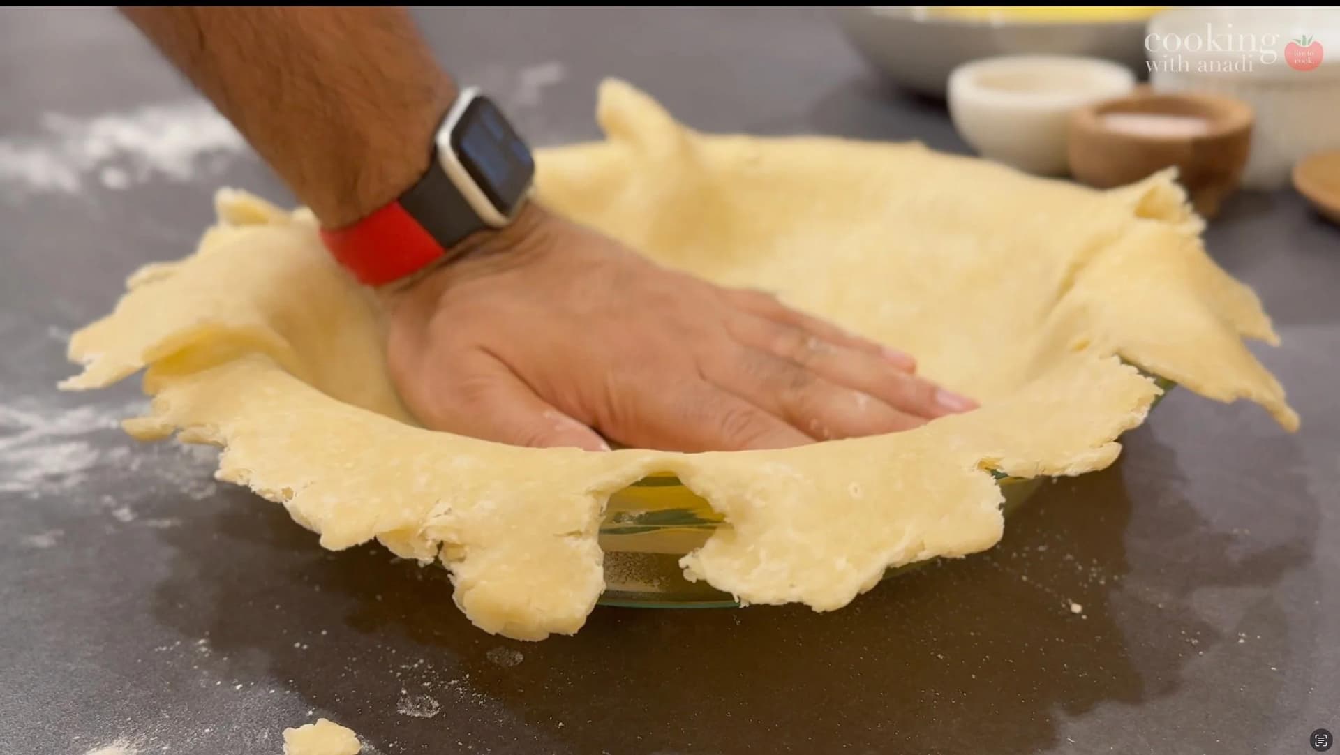 Hand pressing pie dough into a fluted pie dish with a fork visible inside the crust.