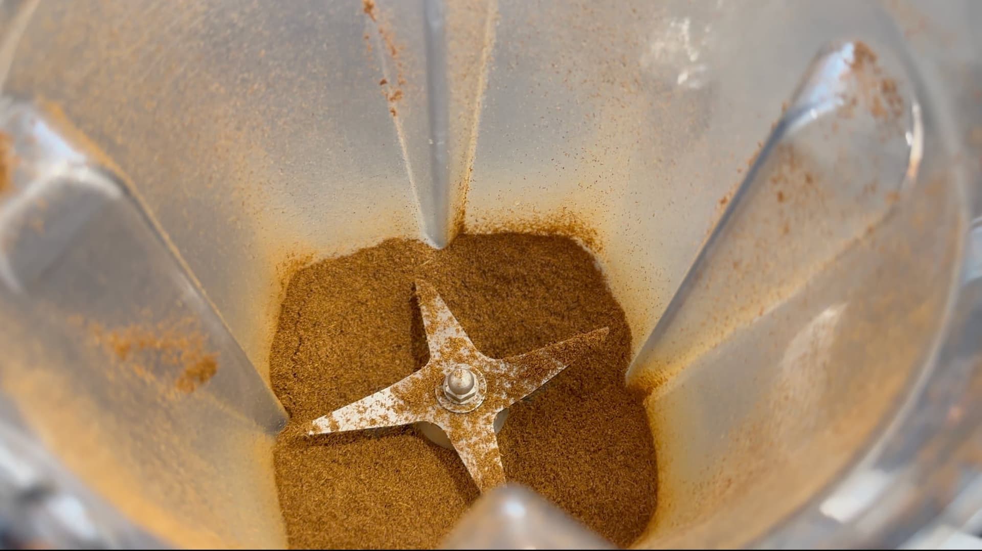 Roasted cumin seeds being ground into powder using a mortar and pestle.