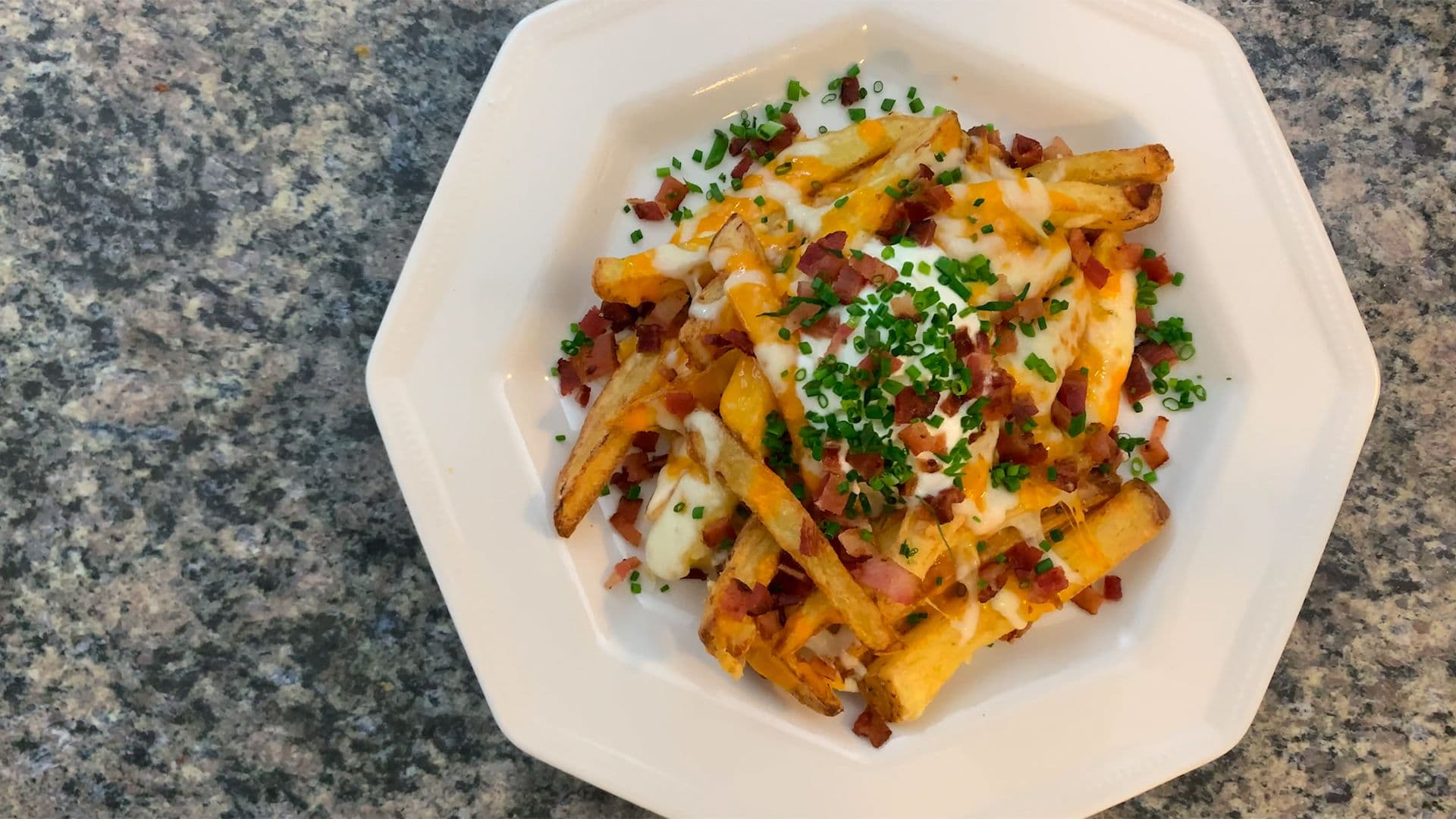Crispy air fryer fries topped with melted cheese, bacon bits, sour cream, and fresh chives on a white plate.
