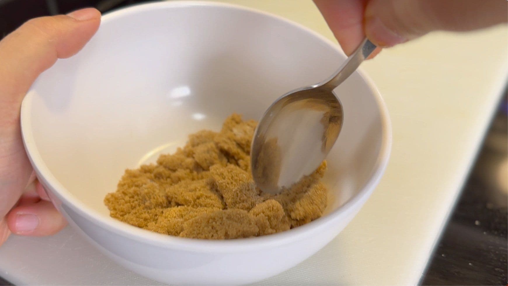 Cinnamon sugar mixture in white bowl being measured with spoon for air fryer cinnamon rolls.