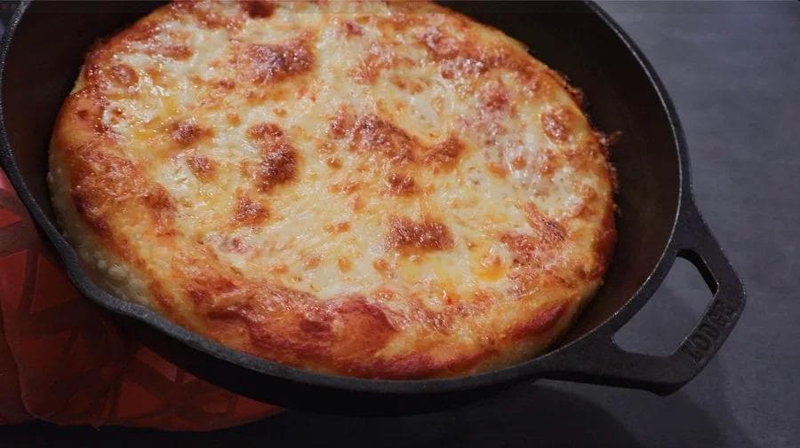 Golden-brown cast iron skillet pizza with melted cheese and crispy crust edges, fresh from the oven.