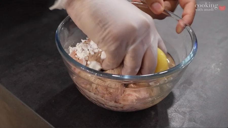 Hand mixing ground chicken mixture with egg and cornstarch in a glass bowl