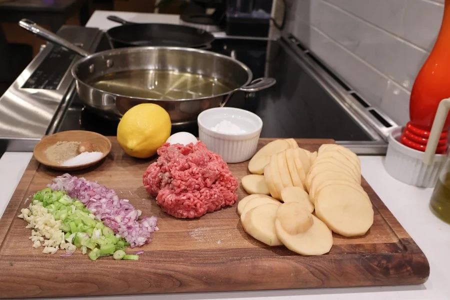 Ingredients for perkedel daging kentang laid out on a cutting board: diced onions, celery, potatoes, ground meat, lemon, and seasonings.