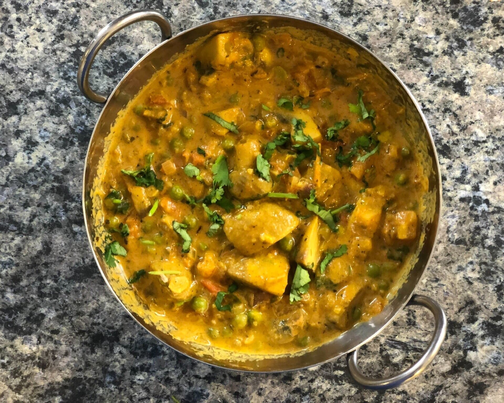 Mushroom matar masala curry in a brass bowl, topped with fresh cilantro, on a granite countertop.