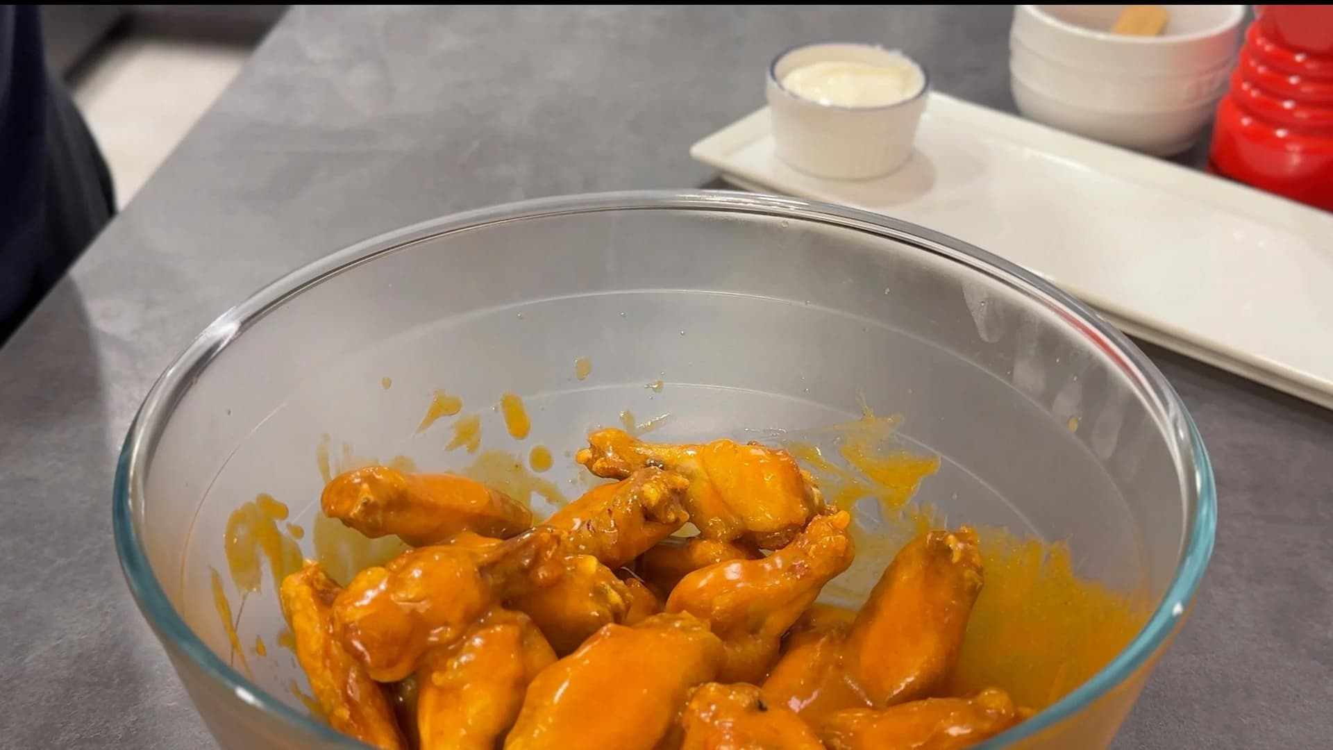 Fried buffalo chicken wings coated in orange hot sauce in a glass bowl, ready to be tossed.