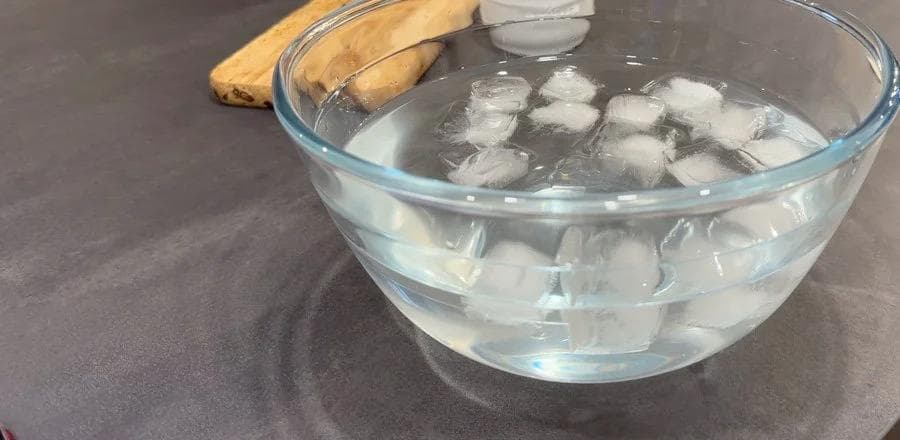 Ice water bath with spinach blanching in a glass bowl beside fresh spinach leaves