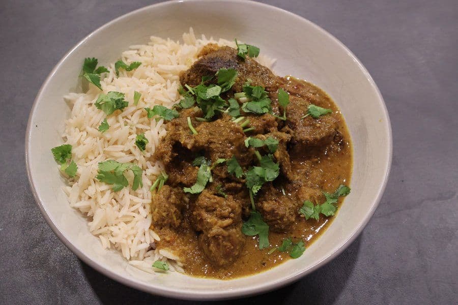 Balinese beef rendang served in a white bowl with steamed rice and fresh cilantro garnish.