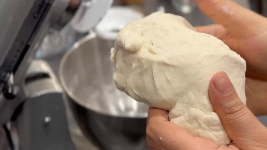 Hands kneading smooth, pale dough on a work surface during bread preparation.