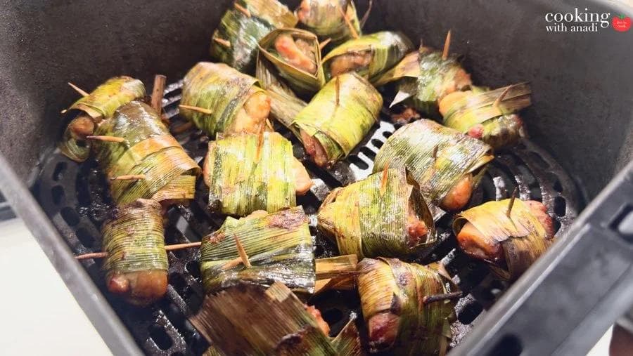 Pandan-wrapped chicken pieces cooked in an air fryer basket, secured with toothpicks, leaves charred and darkened.