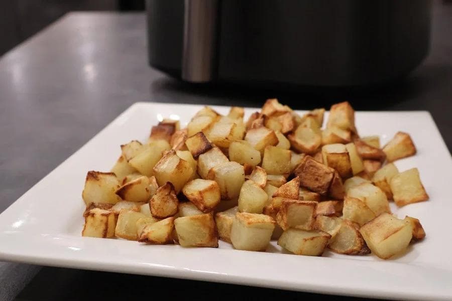 Crispy golden cubed potatoes served on a white plate, cooked in an air fryer.