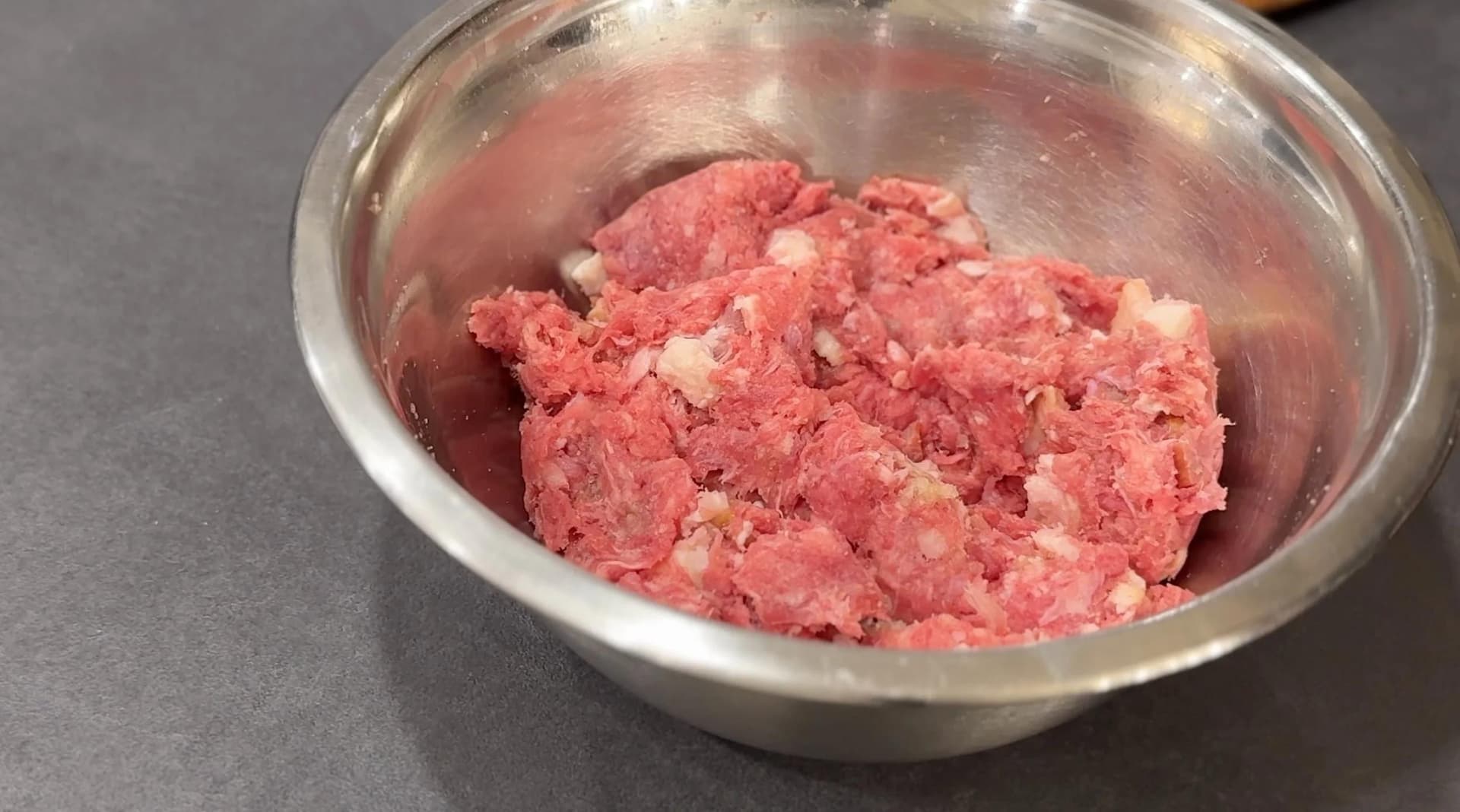 Ground beef mixed with bacon, garlic, and onion powder in a stainless steel bowl.