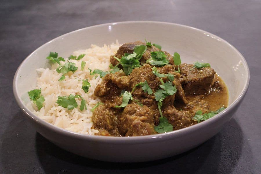 Stovetop Balinese beef rendang served over white rice, garnished with fresh cilantro in a white bowl.
