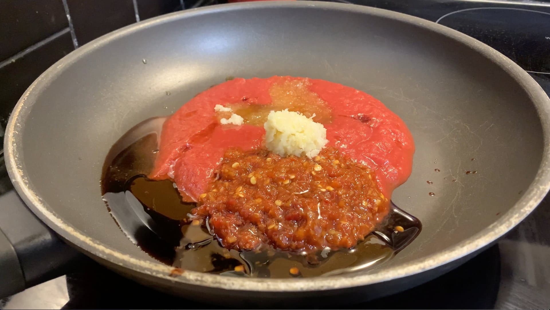 Sauce ingredients simmering in a wok with red sauce, minced garlic, and ginger being cooked together.