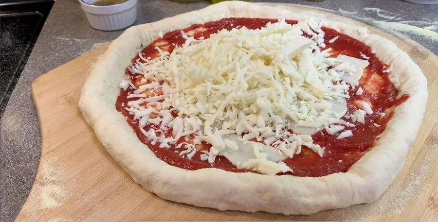Unbaked pizza on parchment with red sauce and shredded mozzarella cheese before baking.