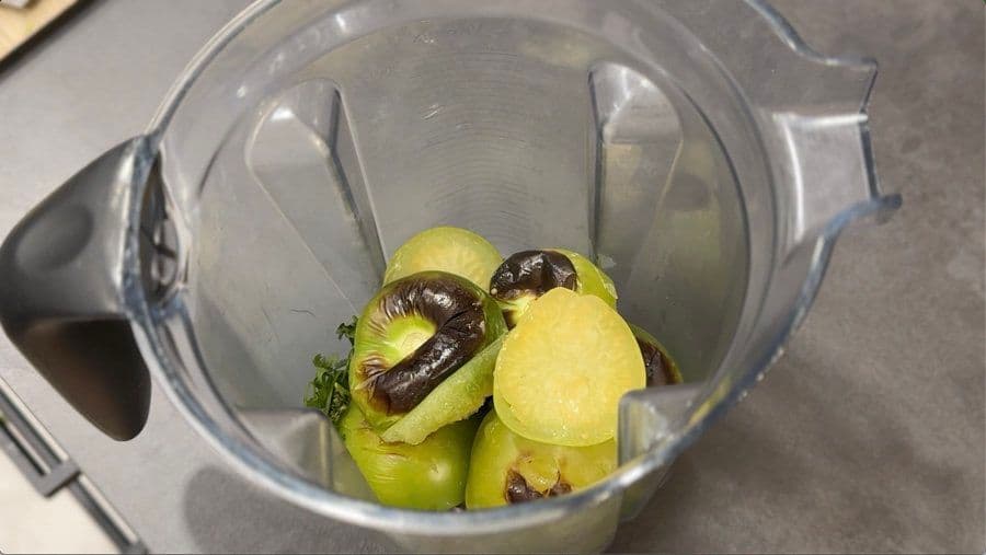 Raw tomatillos and dark chilhuacle peppers in a blender pitcher before blending into salsa verde.