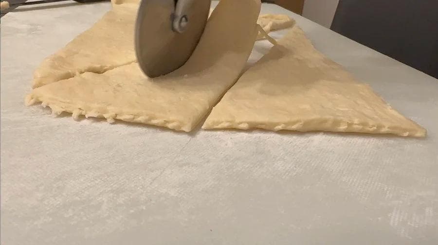 Pizza wheel cutting crescent roll dough into triangular portions on parchment paper.