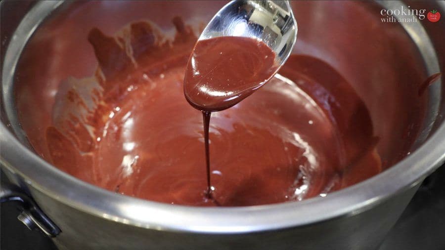 Melted chocolate being dripped from a spatula into a bowl of melted chocolate over a double boiler.
