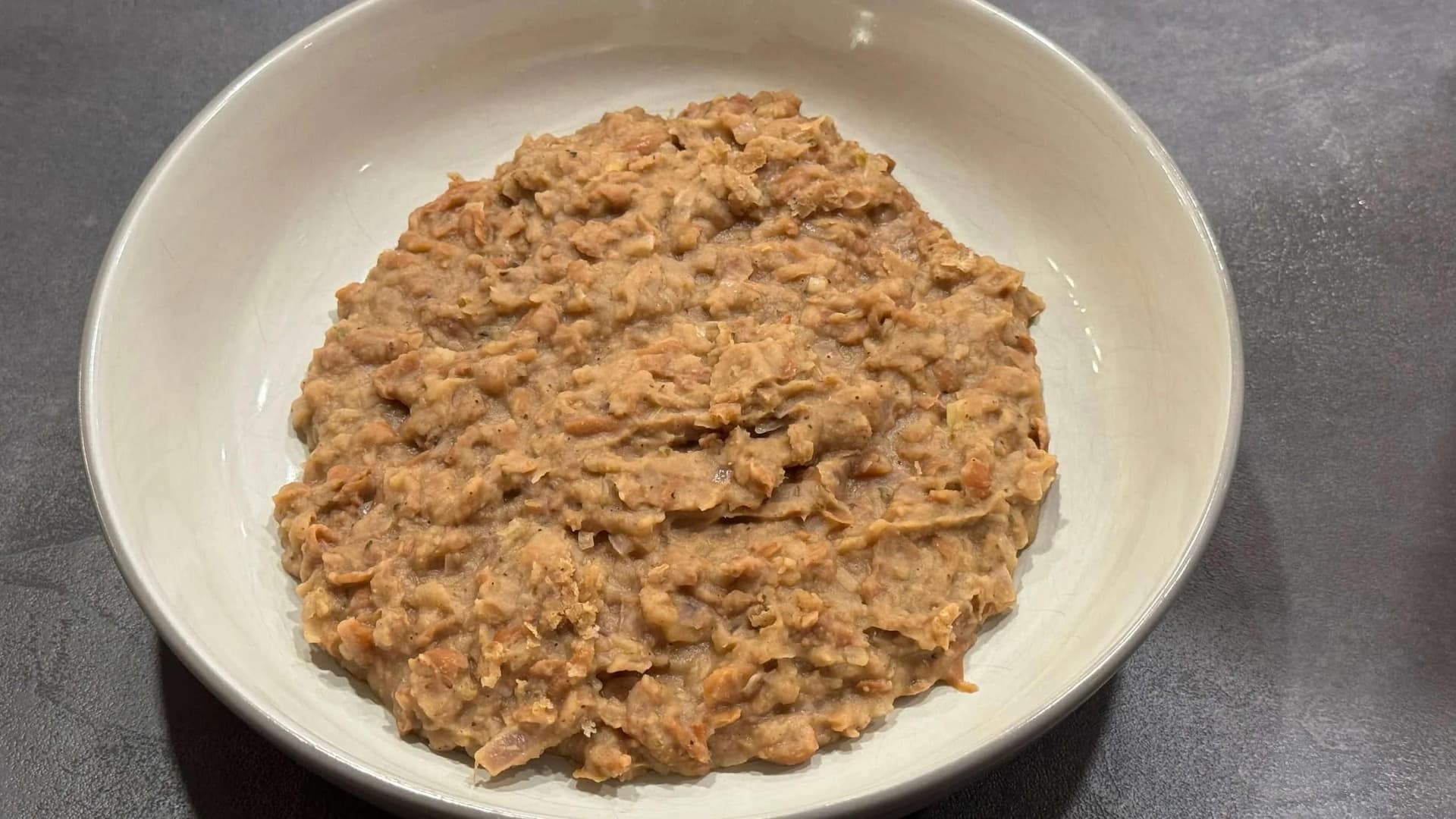 Homemade refried beans in a white bowl with a thick, textured brown consistency.