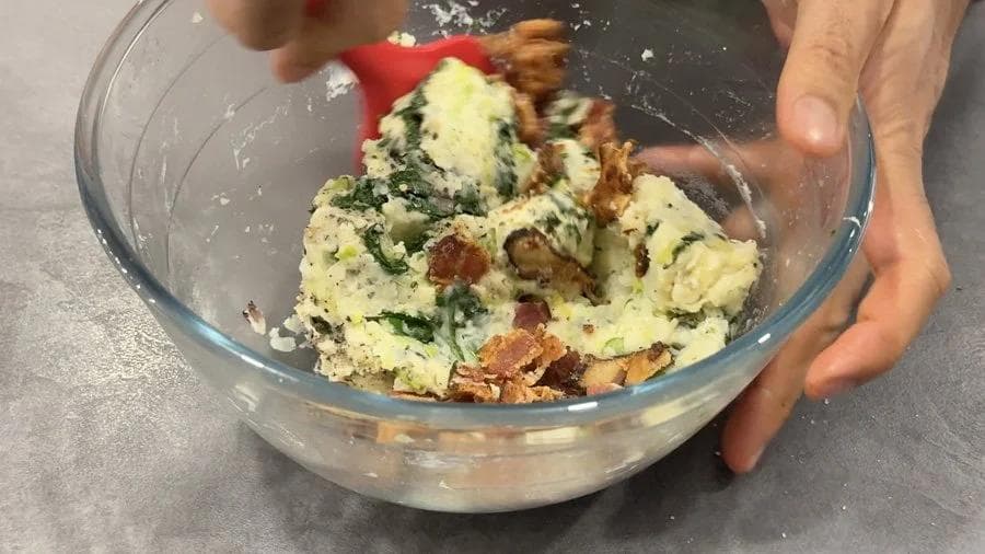 Colcannon potato filling with bacon bits and green herbs mixed in a glass bowl, being prepared for stuffing potato shells.