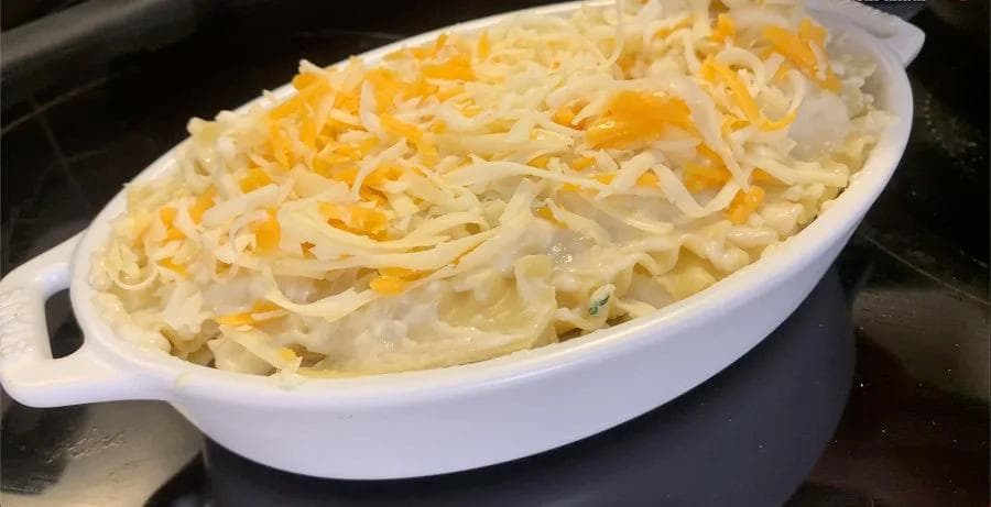 Unbaked lasagna in white oval dish topped with shredded mozzarella and cheddar cheese before baking.