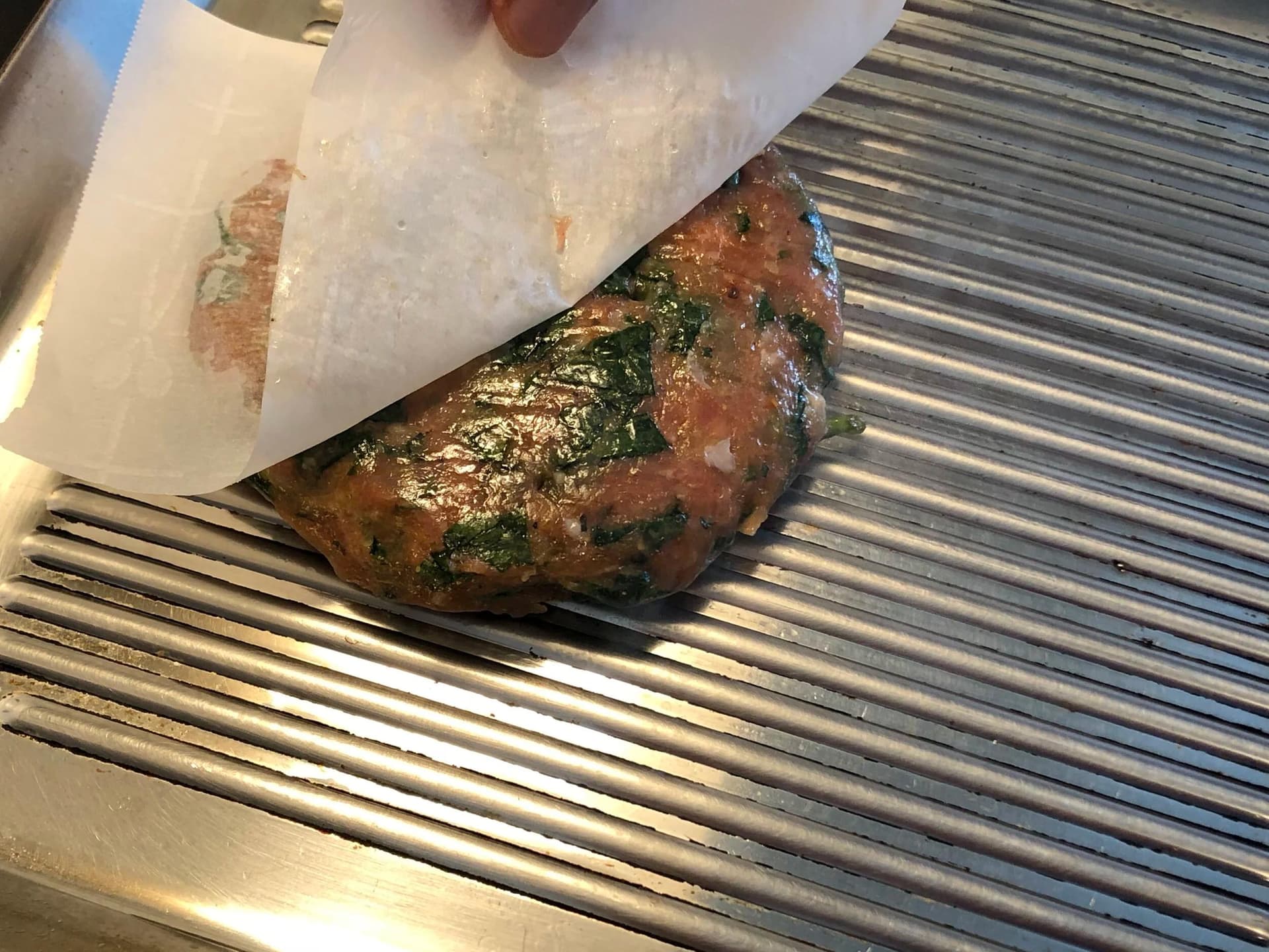 Spinach turkey burger patty with melted cheese on a grill pan, partially wrapped in parchment paper.