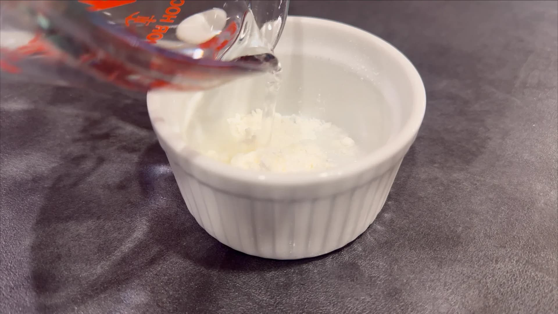 Cornstarch slurry being poured into a white ramekin for thickening meat pie filling sauce.