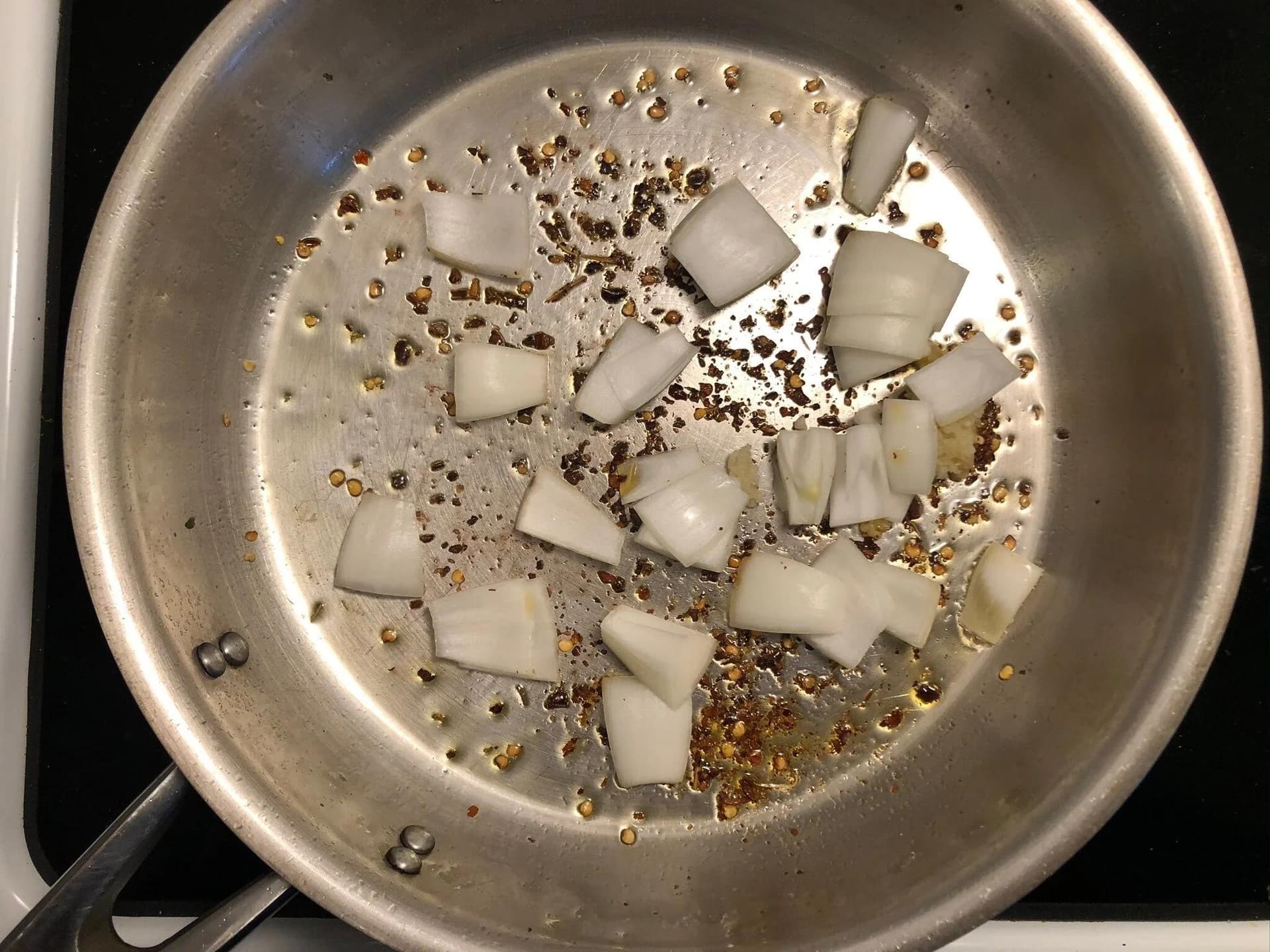 Diced onions and garlic cooking with chili flakes in olive oil in a stainless steel pan.