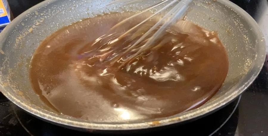 Whiskey caramel sauce being whisked in a saucepan, showing rich brown color and glossy texture.