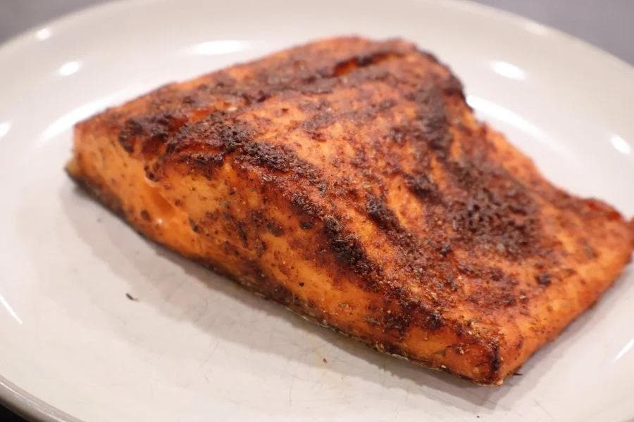 Cooked salmon fillet with crispy skin and seasoning on a white plate