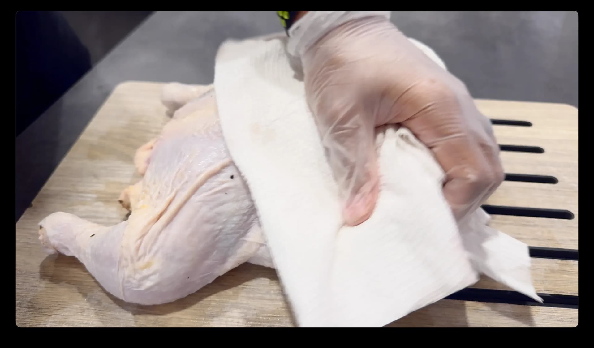 Patting a raw whole chicken dry with paper towels on a wooden cutting board.