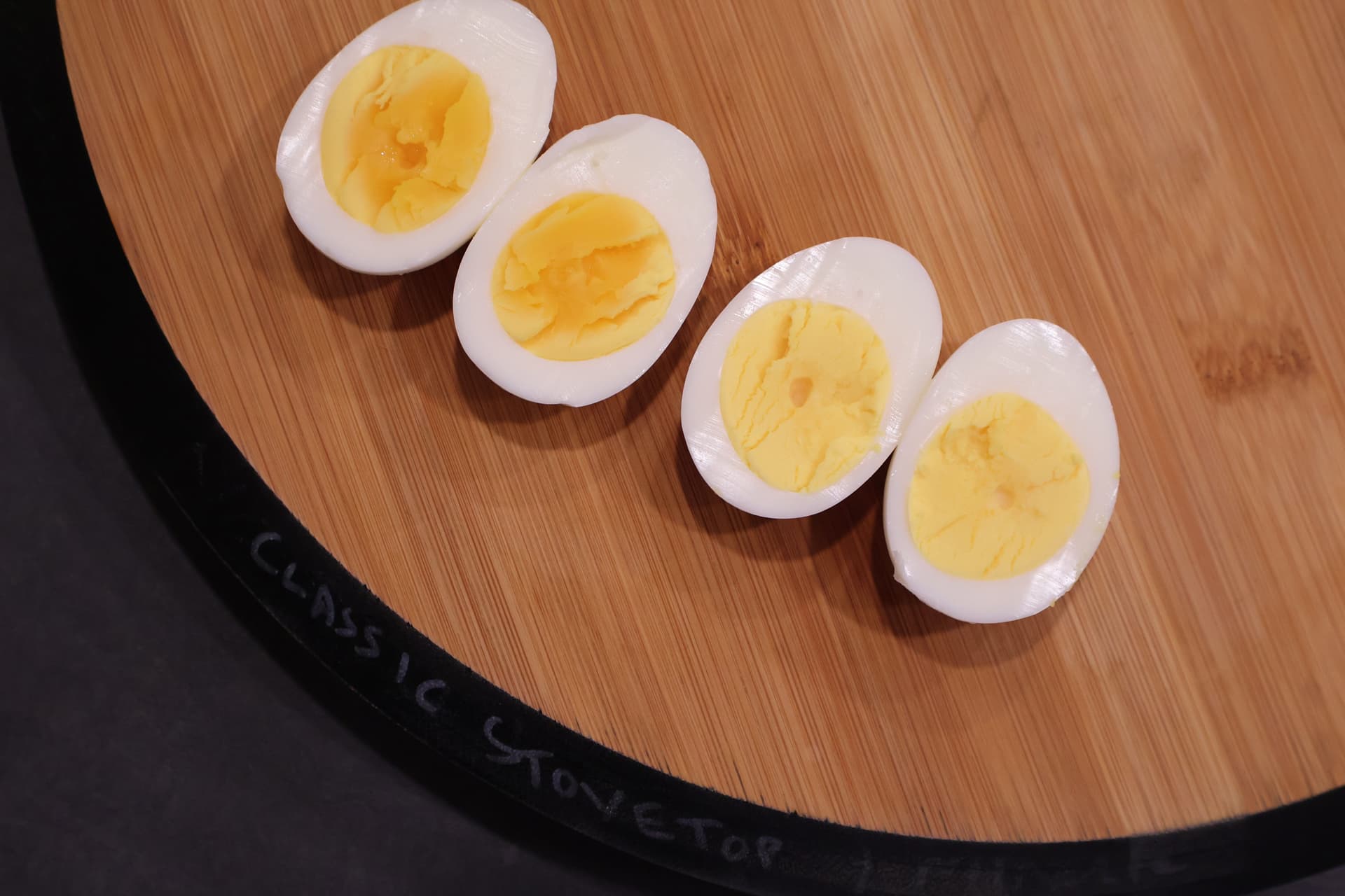 Four halved hard-boiled eggs with cooked yellow yolks arranged on a wooden cutting board.