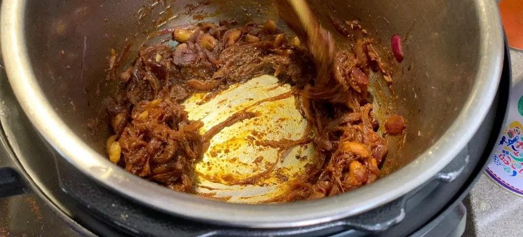 Ginger-garlic paste and spices being added to browned onion masala in an Instant Pot