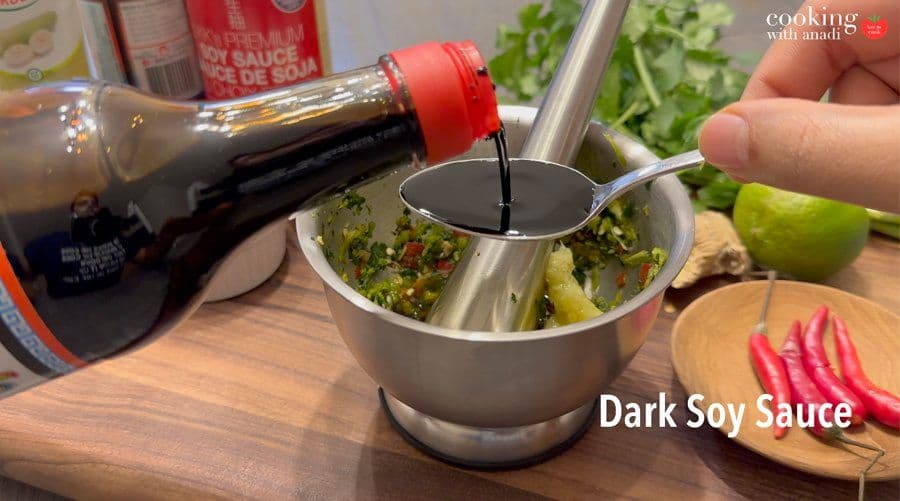 Dark soy sauce being poured from a bottle into a stainless steel bowl containing Thai marinade ingredients.