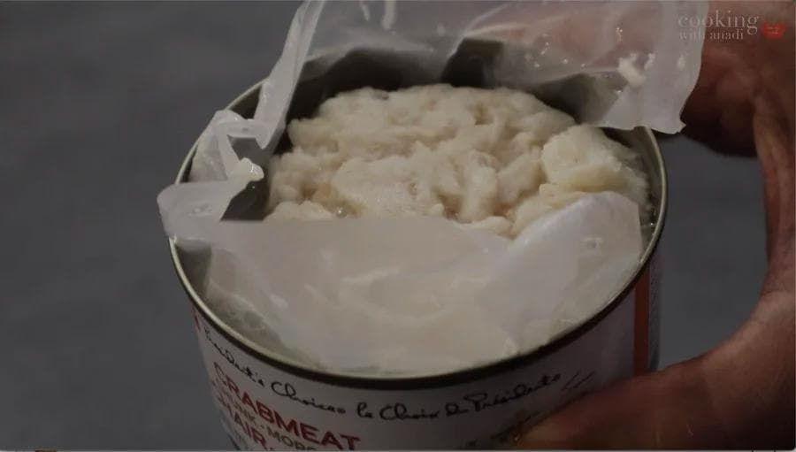 Drained crab meat in a bowl with mayonnaise-based mixture, ready to be combined with other ingredients for crab salad.
