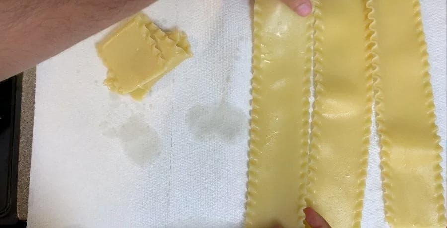 Cooked lasagna sheets cooling on paper towels with a damp towel covering them
