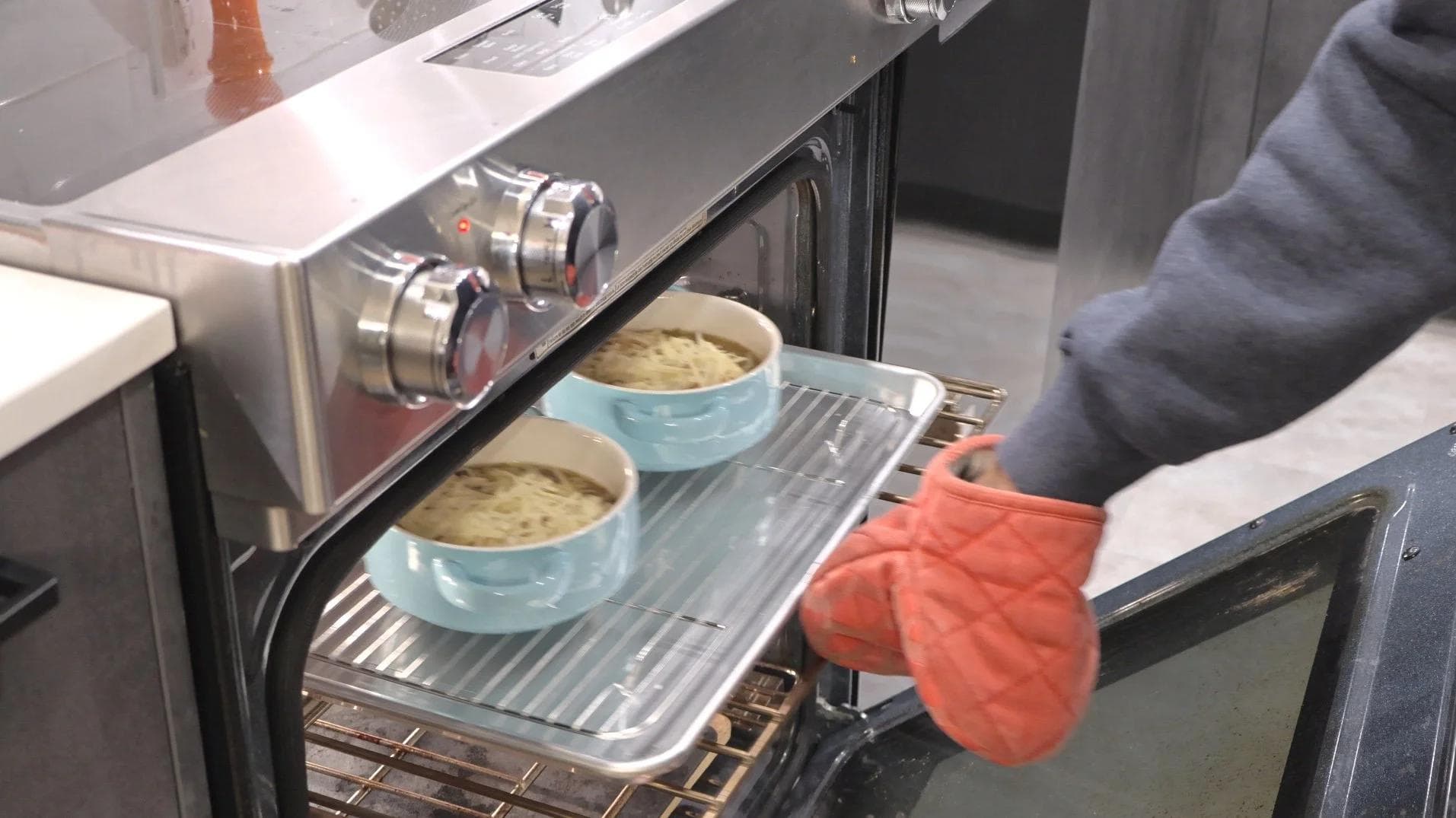 Placing bowls of French onion soup with melted Gruyère cheese into the oven to broil.