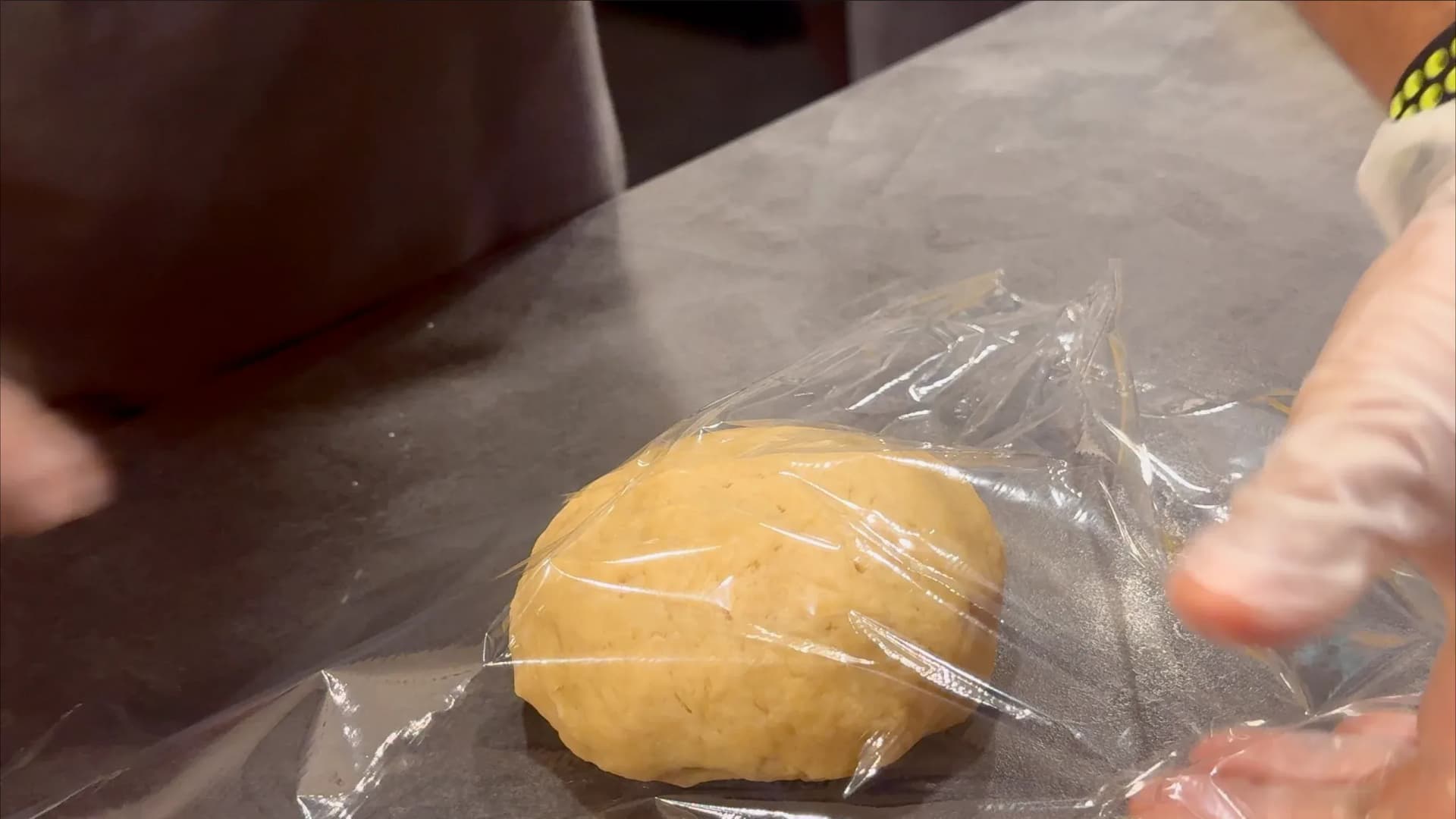 Chilled pie dough ball wrapped in plastic wrap on a gray surface.
