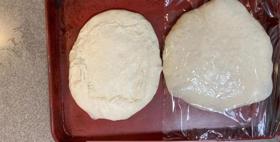 Two pizza dough portions stretched thin on a red baking sheet, ready for stuffed crust filling.