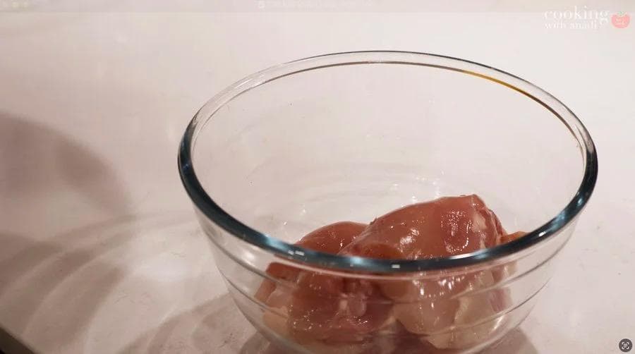 Raw chicken thighs seasoned with salt, oregano, cumin and black pepper in a glass bowl.