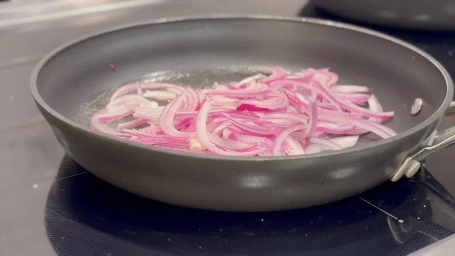 Sliced pink onions sautéing in butter in a gray skillet on a stovetop.