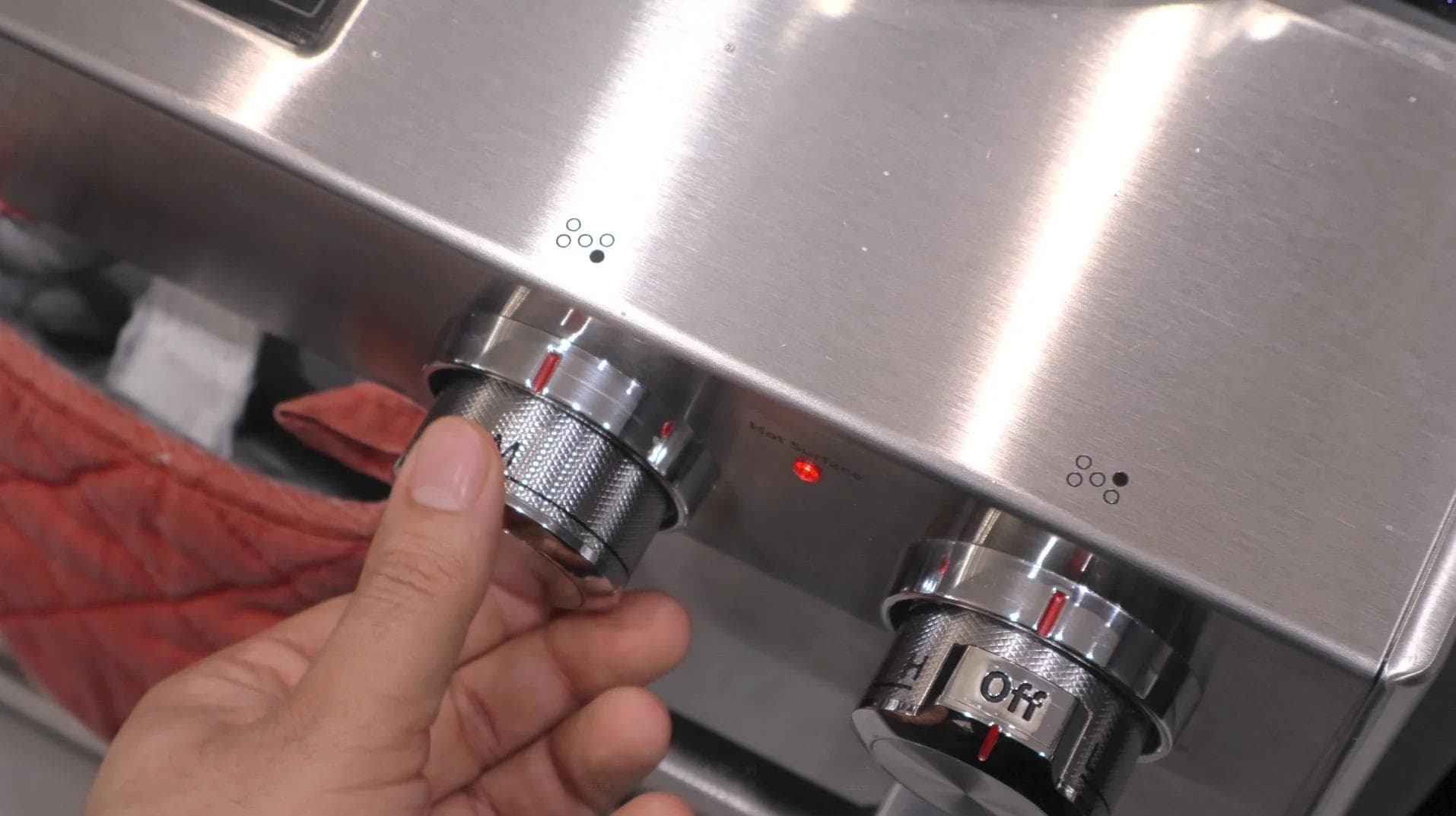 Hand adjusting stovetop burner knobs on a pot during French onion soup preparation.
