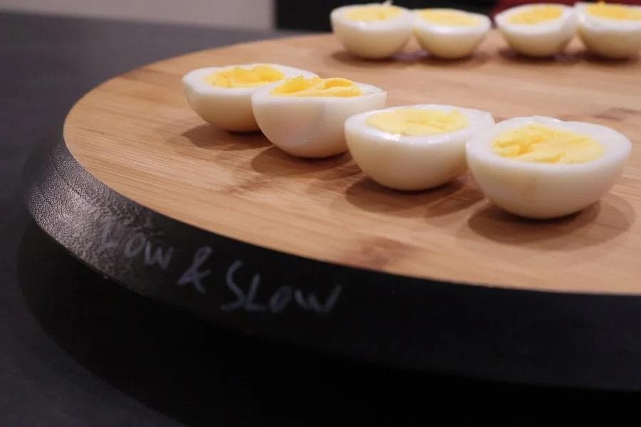 Half-sliced hard-boiled eggs displayed on a wooden cutting board, showing cooked white and yellow yolks.